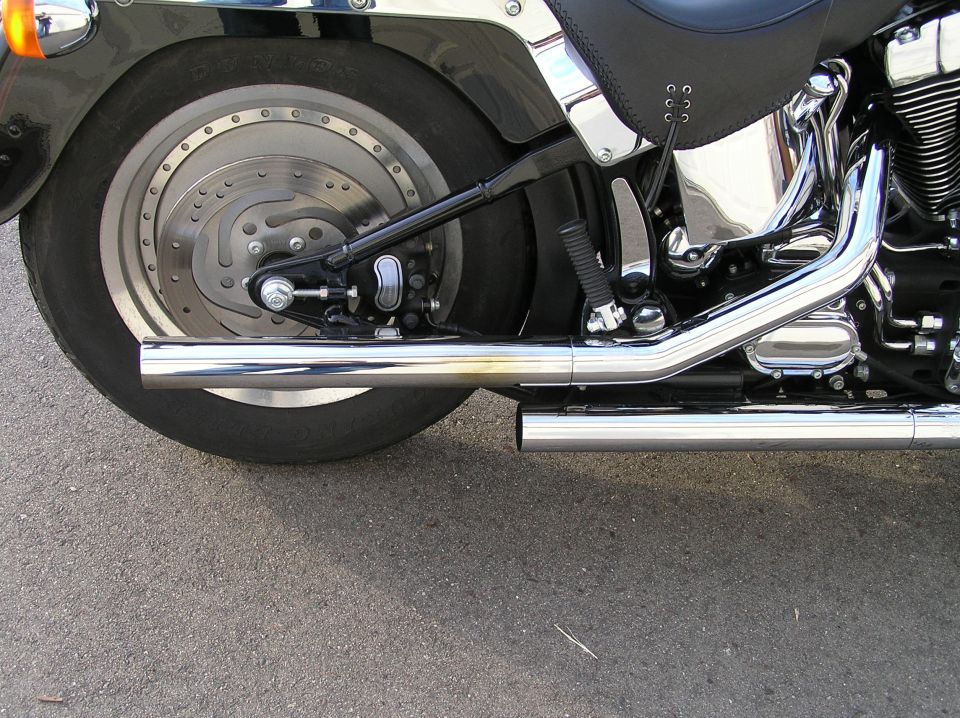 Rear right of black Harley cruiser with chrome dual exhaust and drilled brake rotor