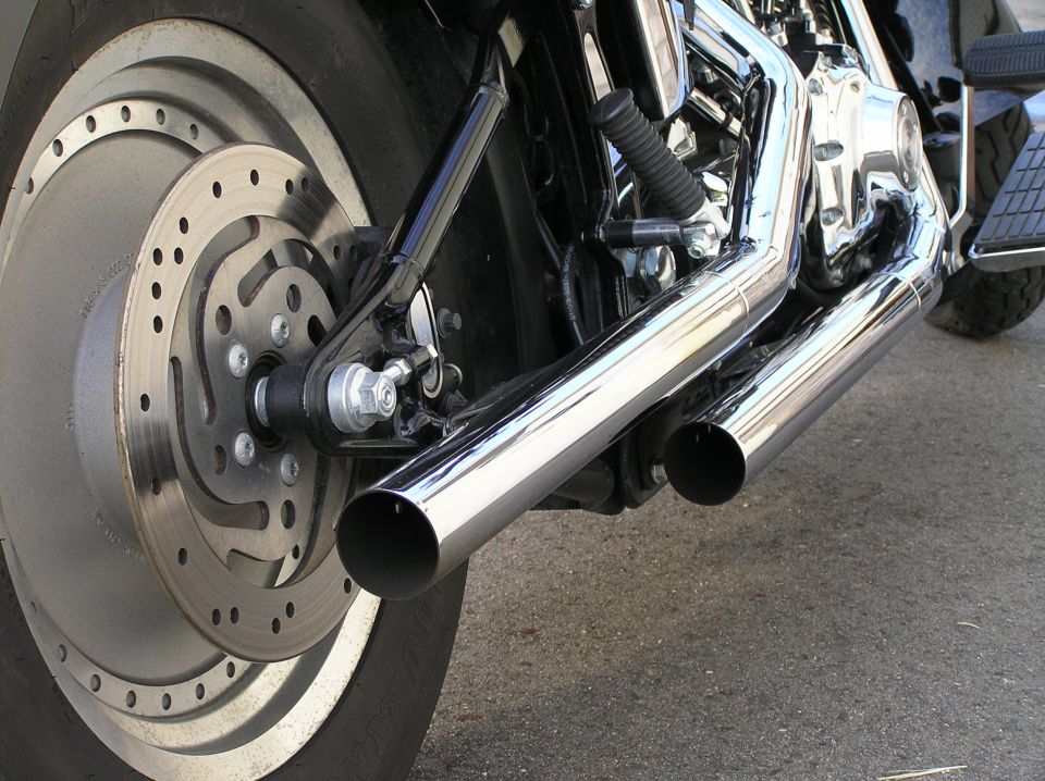 Close-up of motorcycle rear brake rotor and chrome dual exhaust pipes