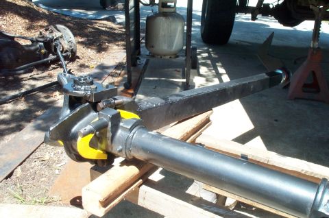 1995 Ford Bronco - Close-up of a black-painted solid axle assembly with a differential yoke, universal joint, and steering knuckle, resting on wooden blocks o…