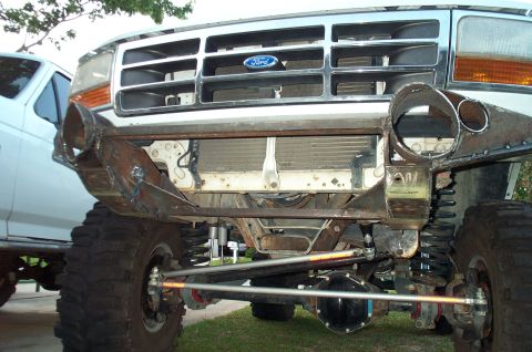 1995 Ford Bronco - Low front view of a lifted white Ford truck with the bumper removed, exposing the solid front axle, coil springs, shocks and heavy Trail Bo…