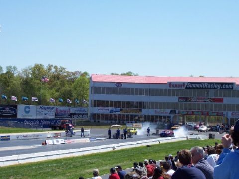 1978 Ford F-250 - Cars are racing down a drag strip with spectators in the stands and a building in the background.