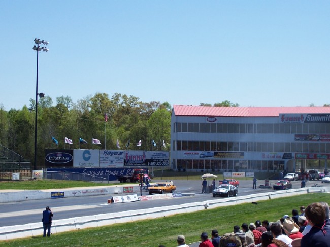 Drag strip scene with cars at the starting line and a grandstand