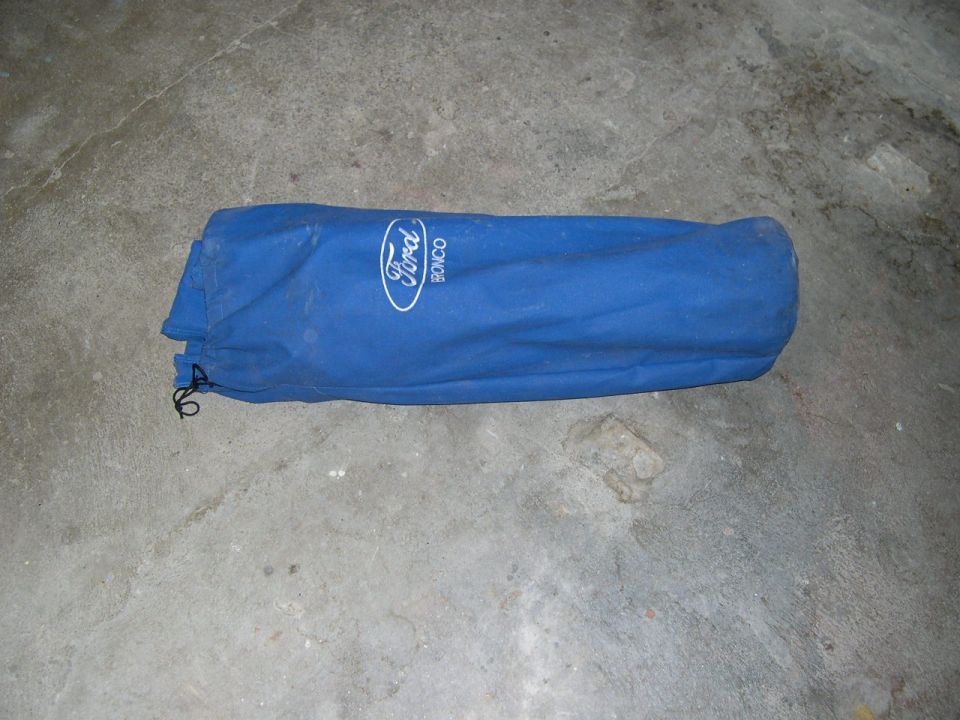 Blue fabric car cover with white Ford Bronco logo, lying on concrete floor