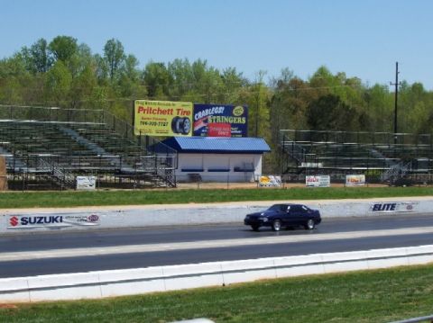 1978 Ford F-250 - A dark blue sedan races down the drag strip, with advertising and bleachers visible.