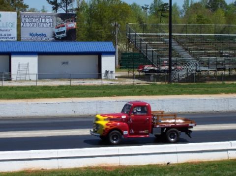 1978 Ford F-250 - A classic red pickup truck with yellow flame graphics on the hood is seen driving on a race track.