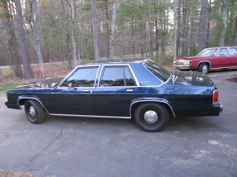 1991 Ford LTD Crown Victoria - A dark blue sedan is parked on a driveway, with a red sedan visible in the background.