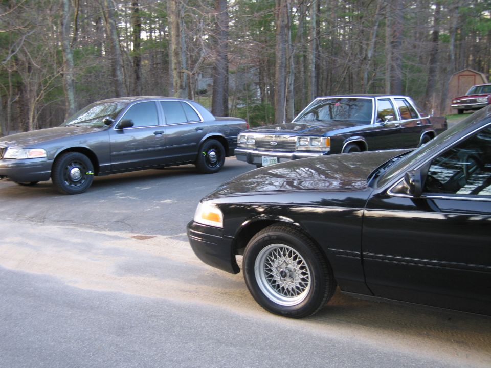 Three Ford Crown Victoria sedans parked on asphalt, one in foreground