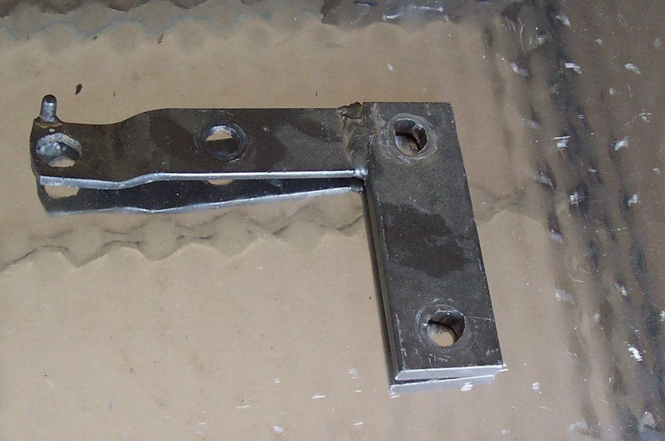 Metal bracket with two mounting holes and a pivot point, on a reflective surface