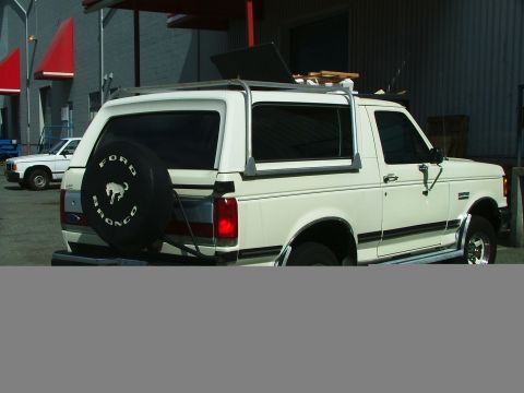 1988 Ford Bronco - This white Ford Bronco is parked outside a building, with a spare tire mounted on the rear door.