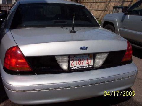 1999 Ford Crown Victoria - A silver Ford Crown Victoria is parked next to another vehicle, showing its rear end and license plate.