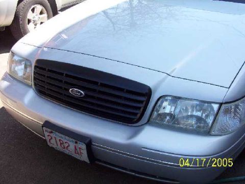 1999 Ford Crown Victoria - Front view of a silver Ford Crown Victoria, showing the grille and headlights. A second vehicle is visible to the left.