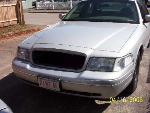 1999 Ford Crown Victoria - Front view of a silver sedan with a missing grille and license plate 2182 AF.
