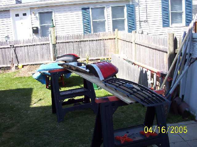 Car grille and red fender on sawhorses in a backyard