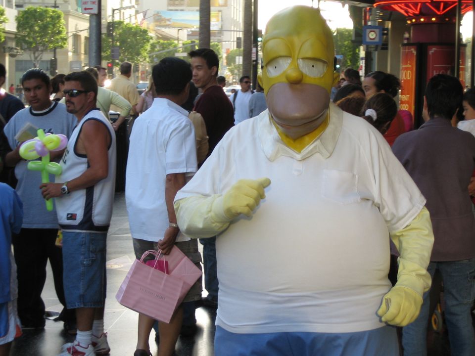guy dressed as Homer Simpson on sidewalk, people around him