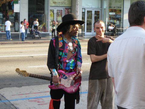 1968 Ford Mustang - A man resembling Jimi Hendrix holds a pink electric guitar while standing on a city sidewalk.
