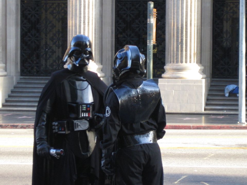 Darth Vader and a stormtrooper stand on a sidewalk in front of a building
