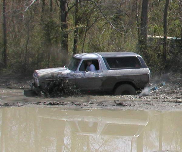 Mud-covered full-size SUV plowing through a muddy pond throwing spray