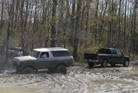 1988 Ford Bronco - Two vehicles are stuck in deep mud in a wooded area, with one person standing near the Bronco.