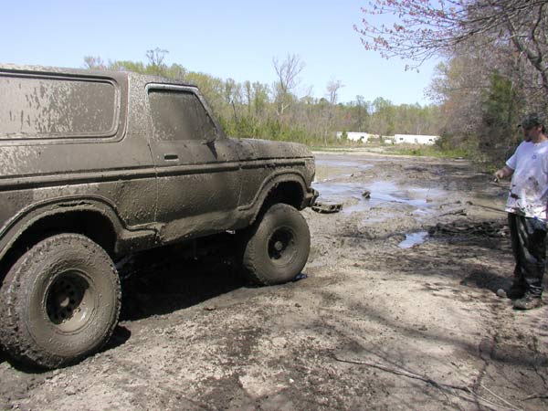 Mud-covered 1978 Ford Bronco parked in a muddy field with a person standing nearby
