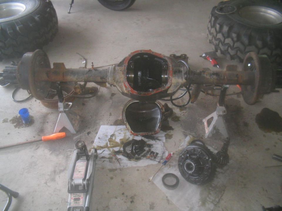Rusty rear axle assembly with differential cover removed, resting on jack stands