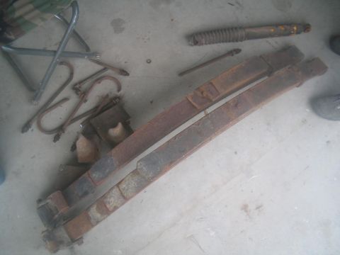 1983 Ford F-250 - Leaf springs and a shock absorber are laid out on a concrete surface, along with various mounting hardware.