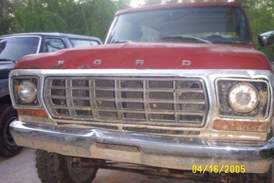 1979 Ford F-150 front grille and bumper, red hood with 'FORD' lettering. Another vehicle is partially visible to the left