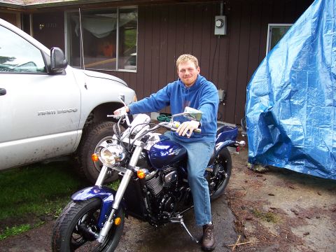 1983 Ford Bronco - A man sits on a blue motorcycle beside a silver truck, with a blue tarp covering something in the background.