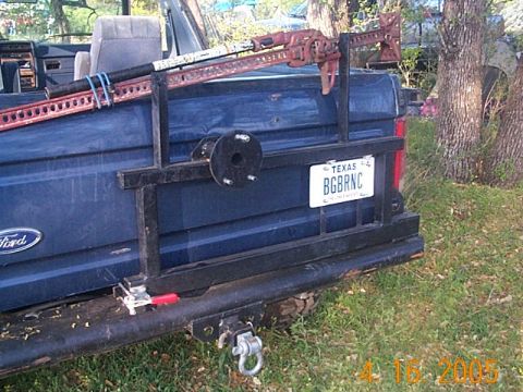 1986 Ford Bronco - The rear of a blue Ford Bronco is shown with a spare tire mount and a Hi-Lift jack attached to a custom rack.