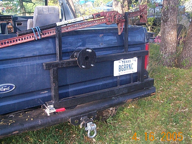 Rear of a blue 1986 Ford Bronco with a custom rack holding a Hi-Lift jack and spare tire mount. Texas license plate reads BGBRNC
