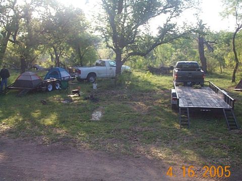 1986 Ford Bronco - A campsite scene shows two trucks, one towing a trailer with a tent, and another truck on a flatbed trailer.