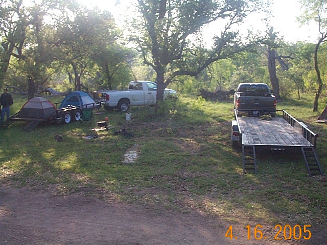Two trucks are parked at a campsite with trailers and tents