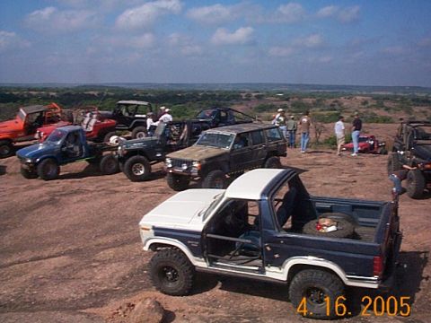1986 Ford Bronco - A group of off-road vehicles are gathered on a rocky terrain under a partly cloudy sky.