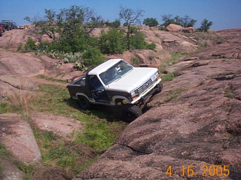 1986 Ford Bronco - 1986 Ford Bronco navigating a rocky off-road course. Another vehicle is visible on the ridge above.
