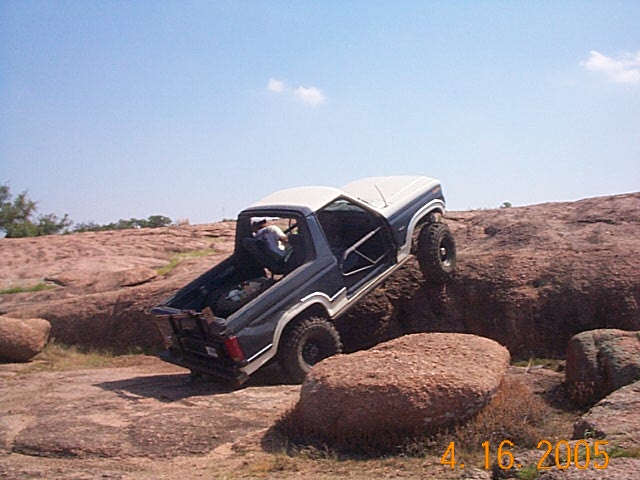 Ford Bronco climbing over rocks, doors removed, spare tire in back