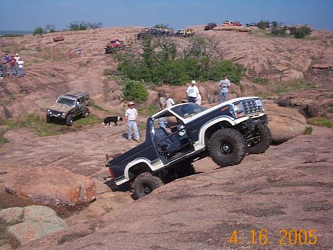 1986 Ford Bronco - Off-road vehicle navigating a steep, rocky terrain with spectators present.