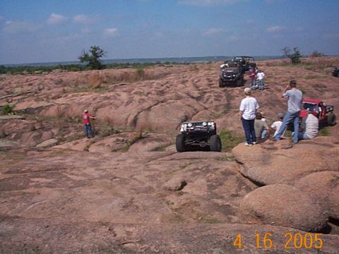 1986 Ford Bronco - Off-road vehicles navigate a challenging rocky terrain, with spectators observing the action.