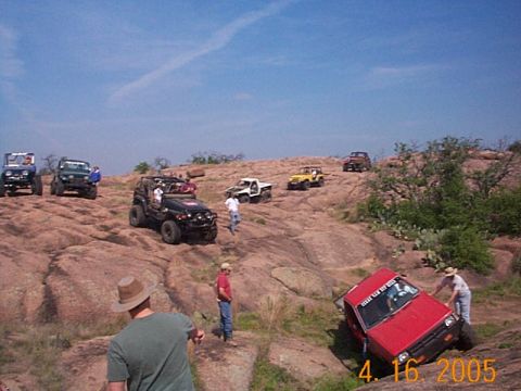 1986 Ford Bronco - Several off-road vehicles navigate a rocky landscape under a clear blue sky.