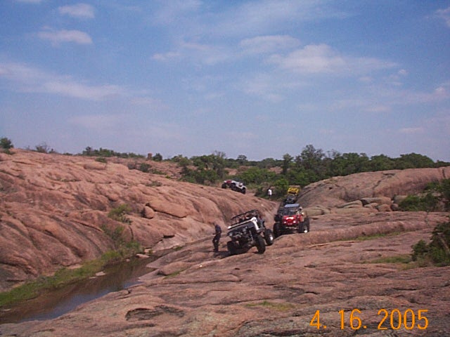 Off-road vehicles climbing a rocky hill under a blue sky