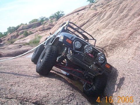 1986 Ford Bronco - Modified Jeep Wrangler navigating difficult rocky terrain, with a tow rope connected.