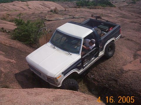 1986 Ford Bronco - This Ford Bronco is navigating a rocky terrain, with its driver visible through the open door.