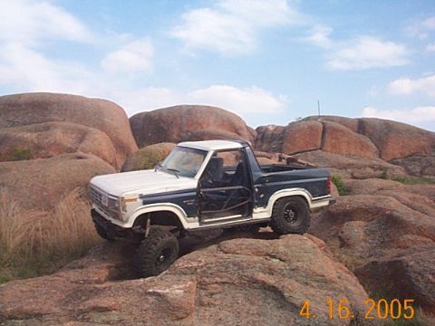 1986 Ford Bronco - A modified Ford Bronco navigates a rocky terrain under a cloudy sky.