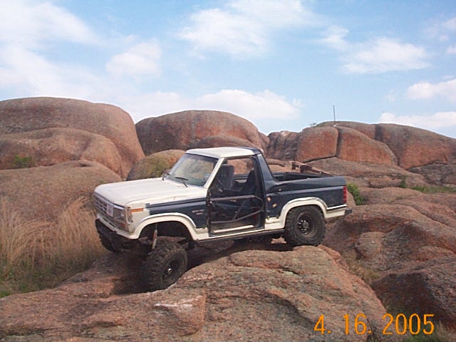 Two-tone blue and white Ford Bronco with roll cage, off-roading on rocks