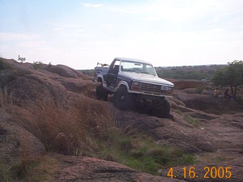 1986 Ford Bronco - A lifted blue pickup truck navigates a rocky landscape, its off-road capabilities.