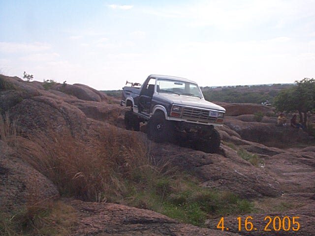 Blue pickup truck with lifted suspension climbing rocks