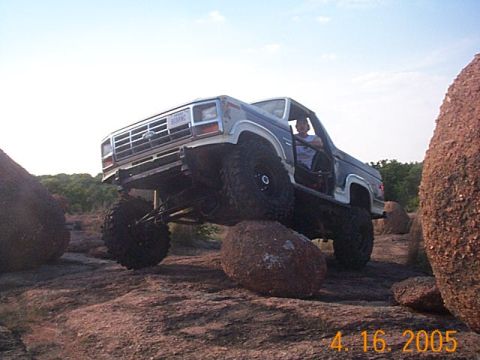 1986 Ford Bronco - A lifted Ford Bronco navigates a rocky terrain, demonstrating its off-road capabilities.