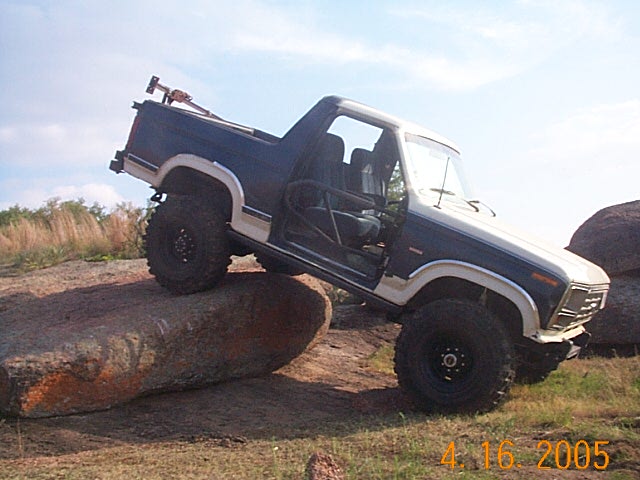 Ford Bronco with off-road tires climbing over large rocks, doors open