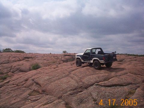 1986 Ford Bronco - A Ford Bronco is parked on a large expanse of pinkish-brown rocks under a cloudy sky.