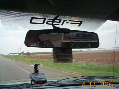 1986 Ford Bronco - Rearview mirror shows reflection of a Ford truck grille; air freshener hangs below.