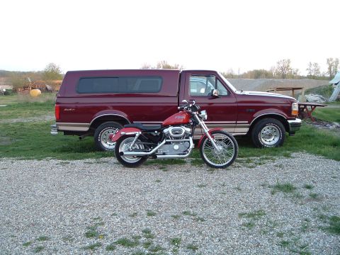 2002 Harley-Davidson Sportster Custom - A red 2002 Harley-Davidson Sportster Custom is parked next to a maroon pickup truck.