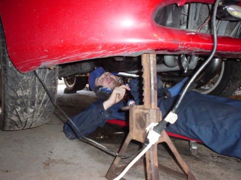 1996 Ford Probe - A person works on the underside of a red vehicle, which is raised on jack stands.